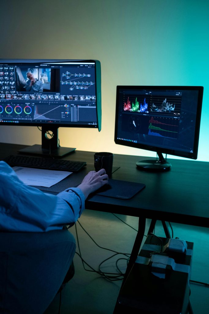 A video editor works on dual monitors in a modern setup, focusing on color grading and editing visuals.